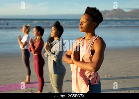 Group of diverse female friends practicing yoga, at the beach standing with eyes close Stock Photo