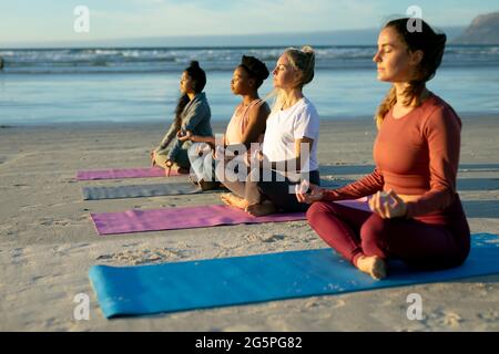 Group of diverse female friends practicing yoga, meditating at the beach Stock Photo