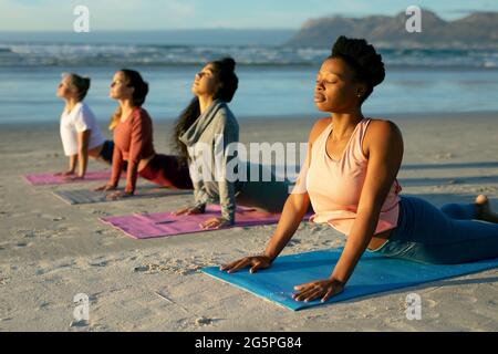 Group of diverse female friends practicing yoga, at the beach laying and starching with eyes close Stock Photo