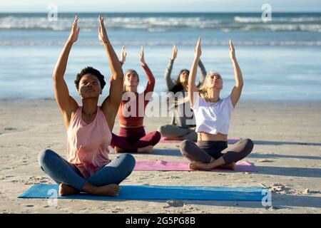 Group of diverse female friends practicing yoga, meditating at the beach Stock Photo
