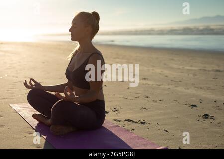Caucasian woman practicing yoga, sitting meditating at the beach Stock Photo