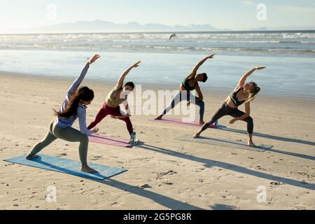 Diverse group of women practicing yoga, standing stretching at the beach Stock Photo