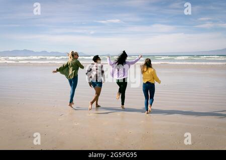 Happy group of diverse female friends having fun, walking along beach Stock Photo