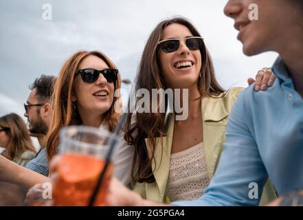 Group of young friends sitting on a bench having fun drinking cocktails, talking, joking together Stock Photo
