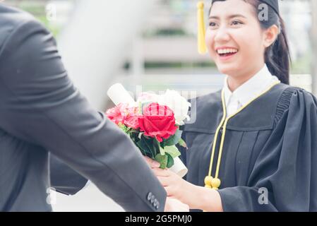 Graduated woman concept. Young smiling woman got flower after finish education. Graduate people finish academy university. Stock Photo