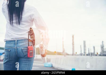 Smart woman engineer holding White safety hard hat helmet for security equipment and blueprint paper working at Petroleum Oil Manufacturing Industry P Stock Photo