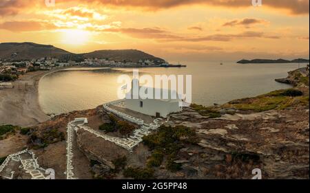 Sunset over Kea Tzia island. Greece, Cyclades. Korissia port and Agios Georgios chapel on a rocky hill, drone, aerial view. Rippled sea, dramatic sky. Stock Photo
