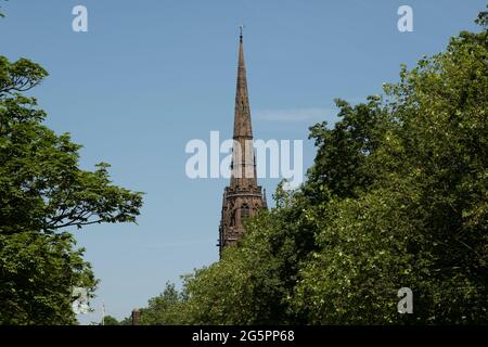 The spire of Coventry Cathedral amongst trees also known as St Michaels, a 14th-century Gothic church, on 23rd June 2021 in Coventry, United Kingdom. The Cathedral Church of Saint Michael, commonly known as Coventry Cathedral, is the seat of the Bishop of Coventry and the Diocese of Coventry within the Church of England. The cathedral lies in ruins and remains a ruined shell after its bombing during the Second World War. Stock Photo