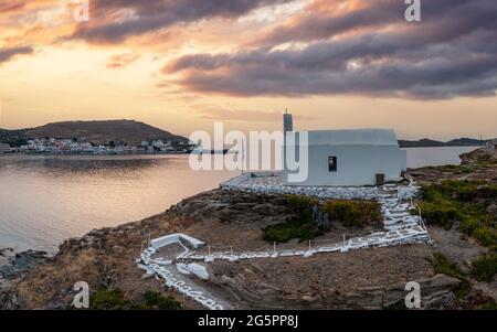 Sunset over Kea Tzia island. Greece, Cyclades. Korissia port and Agios Georgios chapel on a rocky hill, drone, aerial view. Rippled sea, dramatic sky. Stock Photo