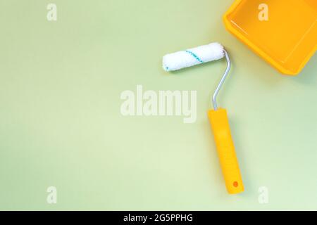 New painting roller and yellow paint tray on pastel green background top view flat lay Stock Photo