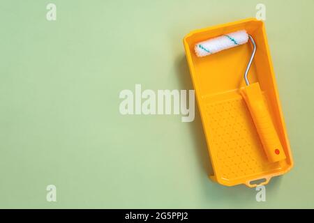 New painting roller in yellow paint tray on pastel green background top view flat lay Stock Photo