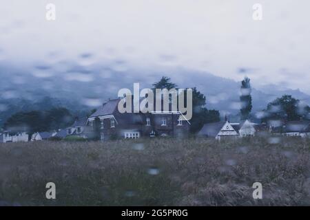 Looking out onto an historic home across a field. As raindrops blur a car window. On a moody summers evening. UK Stock Photo