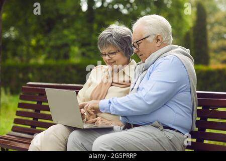 Happy senior couple using a laptop computer while sitting on a park bench together Stock Photo