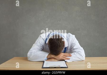 Tired and exhausted male doctor sleeps sitting at a table after a hard day's work. Stock Photo