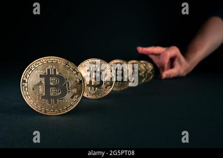 Concept for bitcoin crisis, blockchain bans and restrictions. Hand with fingers ready to send golden bitcoins down like dominoes on black background Stock Photo