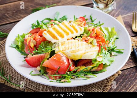 Grilled halloumi cheese salad with salt salmon, tomatoes and green herbs. Healthy food on plate on wooden background. Stock Photo