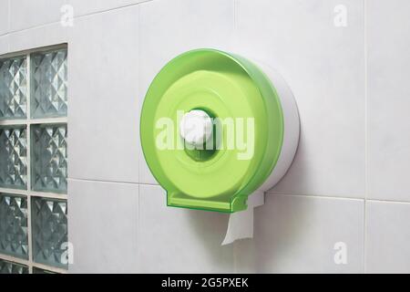 Green plastic toilet tissue paper roll holder with white tissue paper on the tile wall in the bathroom Stock Photo