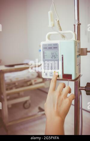 Nurse's hands regulation infusion pump intravenous IV drip in hospital room. Health care under medical observation. Vignette and vintage picture style Stock Photo