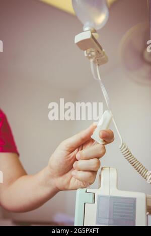 Nurse's hands regulation an intravenous (IV) drip in hospital room. Health care under medical observation. Vignette and vintage picture style. Stock Photo