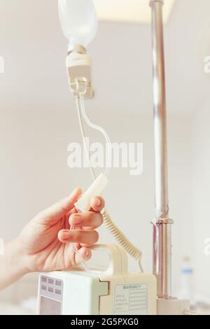 Nurse's hands regulation infusion pump intravenous (IV) drip in hospital room. Health care under medical observation. Vintage picture style. Stock Photo