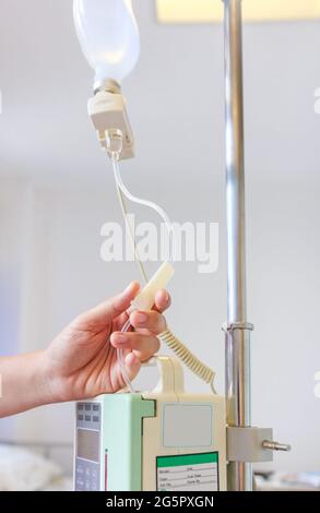 Nurse's hands regulation infusion pump intravenous (IV) drip in hospital room. Health care under medical observation. Stock Photo