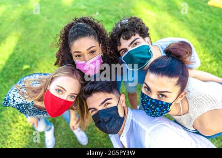 Bright vivid color effect photography of multiracial group of young people looking at camera from bottom wearing colored protective face mask on a gre Stock Photo