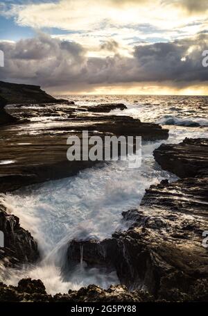 Spectacular sunrise with ocean water crashing and flowing on volcanic rocks off Lanai Lookout, Oahu, Hawaii, USA Stock Photo