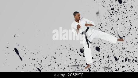 African american male martial artist with black belt against paint splatter on grey background Stock Photo