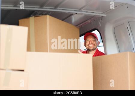 Smiling male courier pulls out cardboard box from car Stock Photo