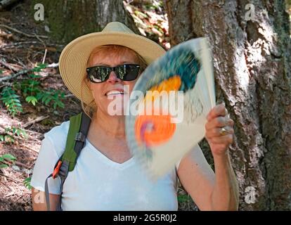 A middle-aged senior citizen using a fan to cool herself while hiking in the Cascade Mountains of central Oregon. Stock Photo