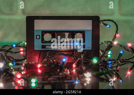 A black Maxell audio cassette is reflected in a glossy black background, illuminated by garlands Stock Photo