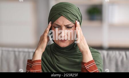 Mature Muslim Woman Suffering From Headache Sitting At Home, Panorama Stock Photo