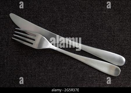 Silver chrome cutlery including a fork facing down and a knife facing inward, clean flatware set on dark grey table cloth, food related concept Stock Photo