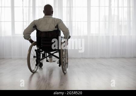 Disabled person sits in wheelchair against window Stock Photo