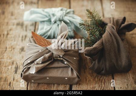 Zero waste stylish christmas gifts. Xmas presents wrapped in fabric with fir branch and leaf on rustic wooden table. Eco friendly winter holidays. Fur Stock Photo