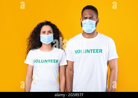 Couple Of Volunteers Wearing Face Masks Over Yellow Studio Background Stock Photo