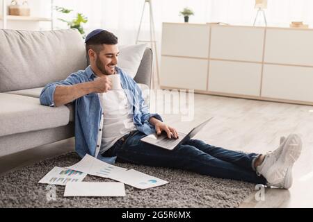 Smiling jewish man watching video on pc, drinking hot coffee Stock Photo