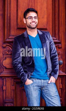 Portrait of Young Scholar. A young man, wearing a dark blue woolen blazer, blue jeans, a blue sweater, glasses, and two hands putting in the pockets, Stock Photo