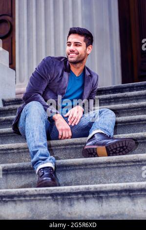Young Man Relaxing Outside. Dressing in a dark purple woolen blazer, blue jeans, and black leather shoes, a young Middle Eastern man with bread is sit Stock Photo