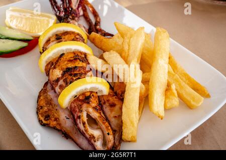 Grilled calamari served with vegetables and fries. Traditional Greek dish. Stock Photo