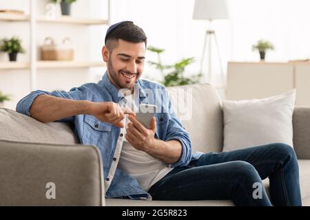 Smiling jew man using smart phone sitting on couch Stock Photo
