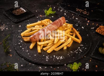 Grilled sausages rolled in bacon served with french fries Stock Photo