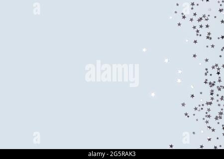 Metallic silver glittering stars confetti scattered on a blue pastel background with copyspace. Stock Photo