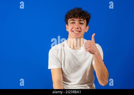 Handsome hispanic model man over isolated background doing happy thumbs up gesture with hand. Approving expression looking at the camera with showing Stock Photo