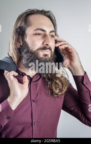 portrait of a young middle eastern businessman with beard and long hair while having a conversation on the mobile phone Stock Photo