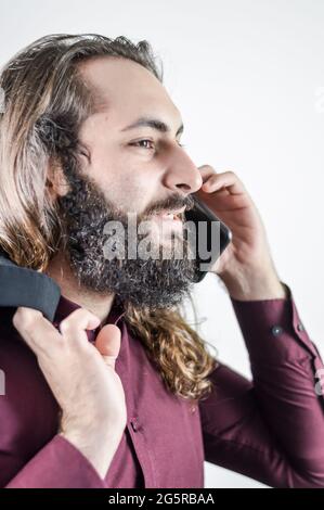 profile portrait of a young middle eastern businessman with beard and long hair while having a conversation on the mobile phone Stock Photo