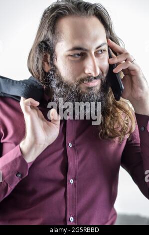 portrait of a young middle eastern businessman with beard and long hair while having a conversation on the mobile phone Stock Photo