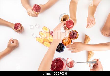 childrens hands holding homemade delicious berries ice cream scoop in waffle cone on white table. Summer healthy dessert Vegan food Stock Photo