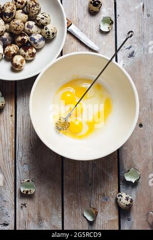 Broken quail eggs in a bowl on a wooden background. Stock Photo