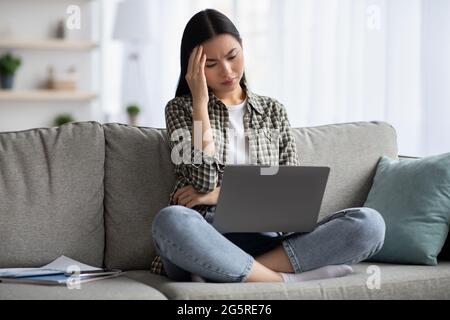 Exhausted korean lady suffering from headache while using laptop Stock Photo